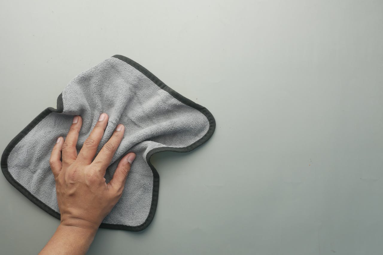 hero-img-02 A hand wipes a light-colored table using a gray microfiber cloth, ideal for cleaning concepts.